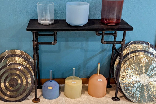 Sound room with crystal singing bowls on a stand, practice bowls, and gongs against a blue wall